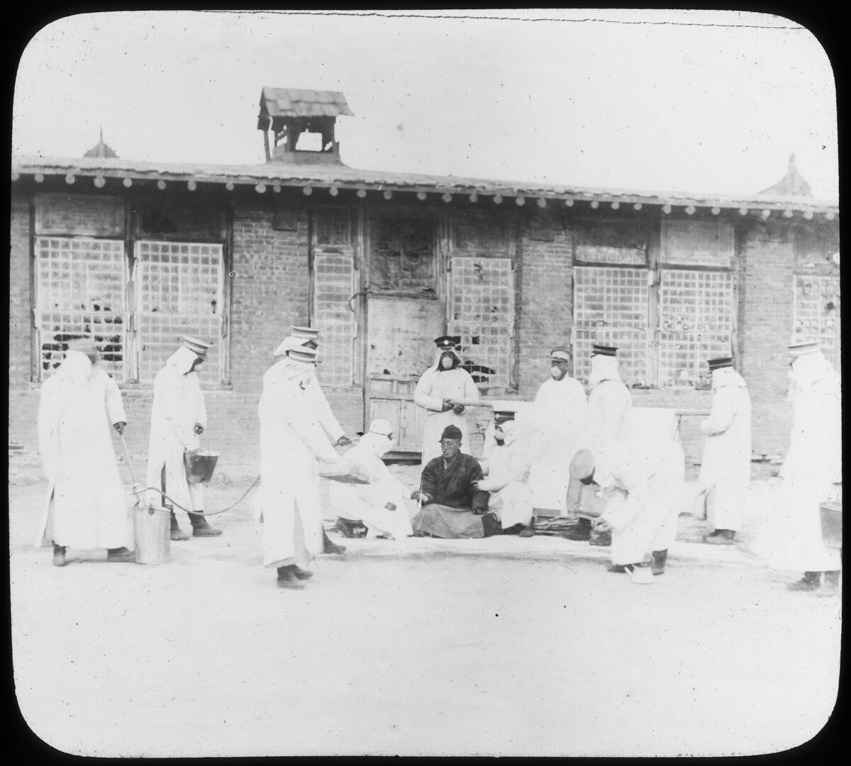 A group of men in white protective robes examine a man sitting on the ground