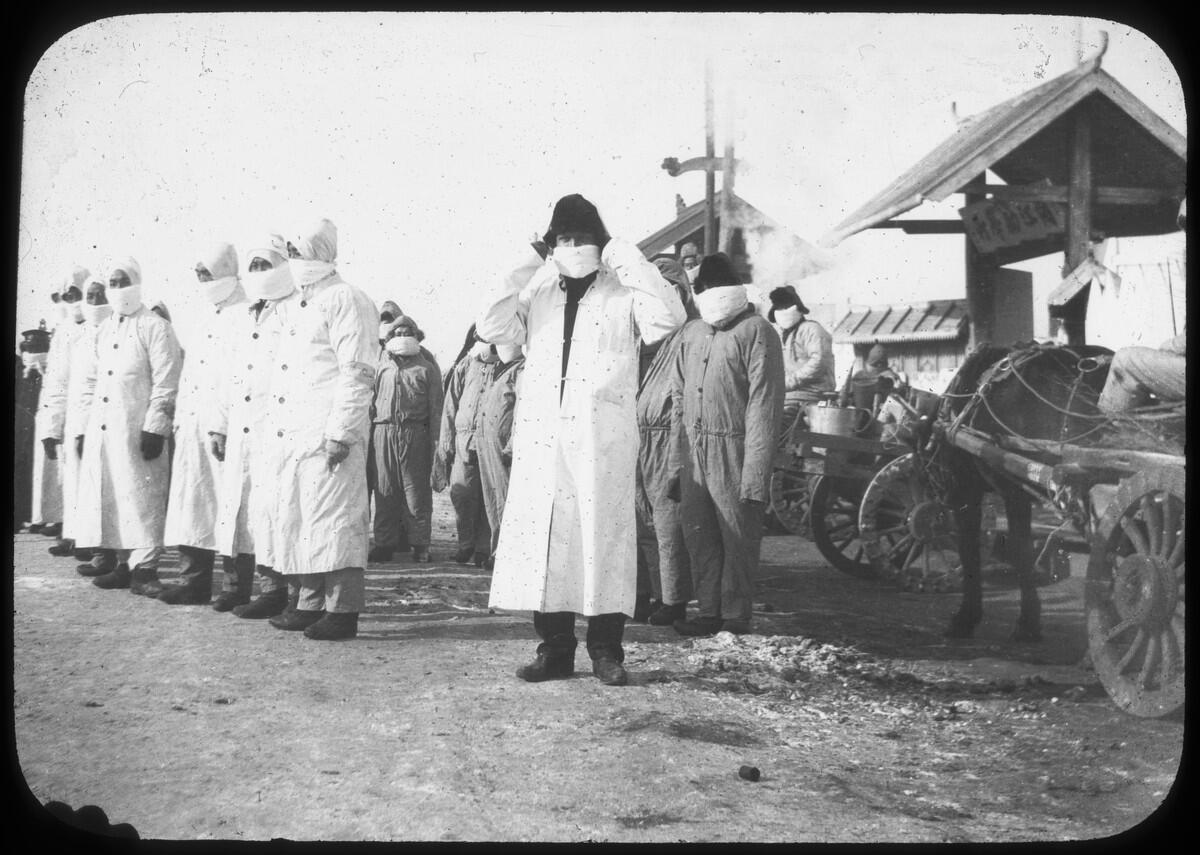 Men in white protective coats stand in front of a horse-drawn cart