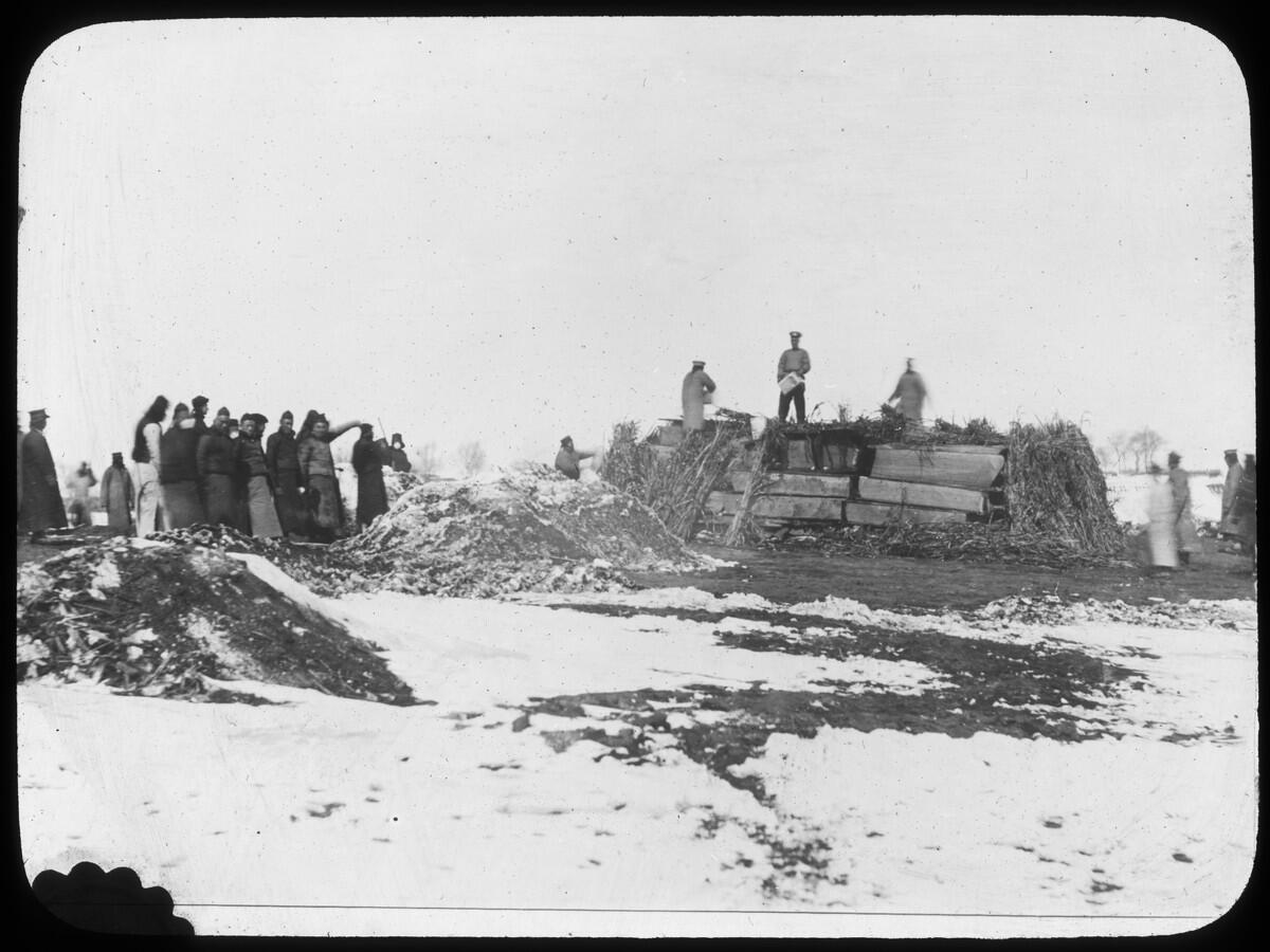 People stand atop a mountain of coffins, spreading kerosene before cremation