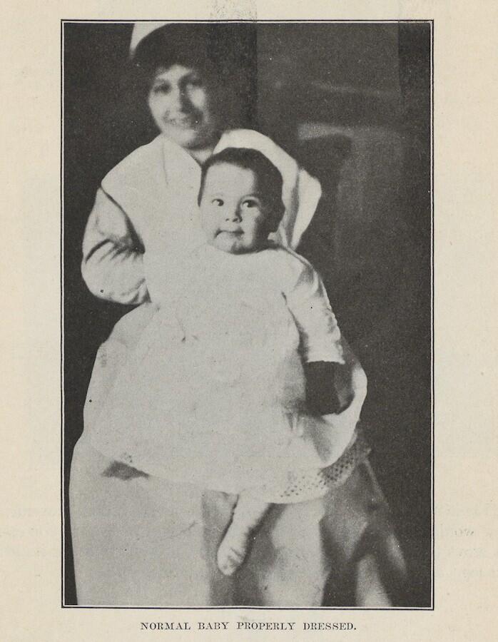 Baby in gown sits on woman's knee