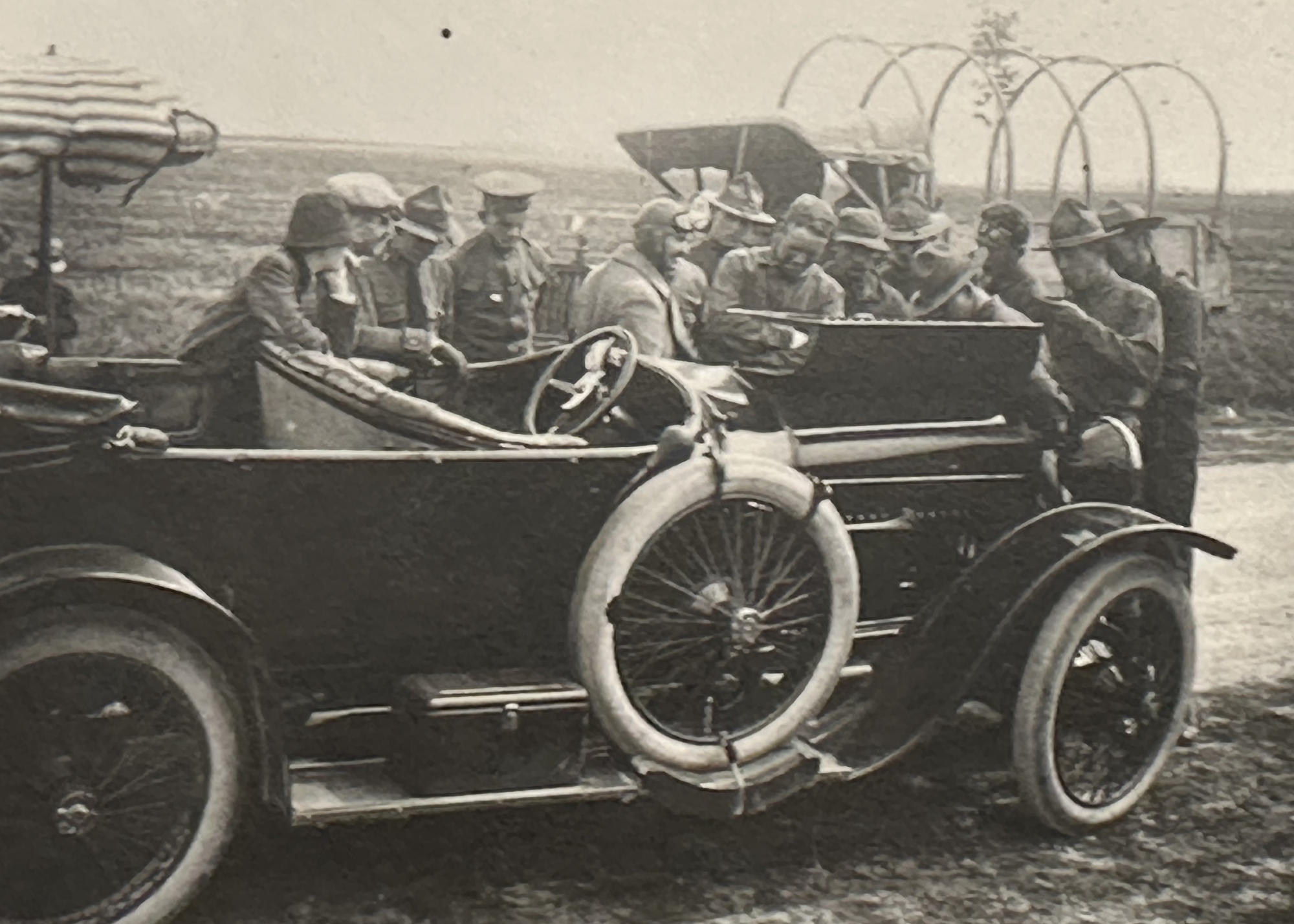 A group of men stands around an open-top car with the motor bonnet open.